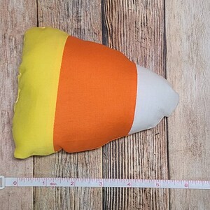 May include: A yellow, orange, and white candy corn shaped pillow. The pillow is about 7 inches long.