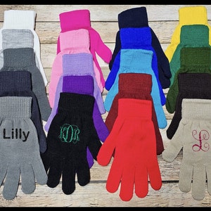 May include: Assortment of 12 pairs of fingerless gloves in various colors, including gray, black, white, pink, purple, blue, red, green, and beige. Some gloves have embroidered names or initials, such as "Lilly", "KOR", and "L".