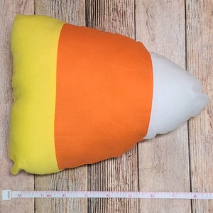 May include: A yellow, orange, and white candy corn shaped pillow. The pillow is about 18 inches long.