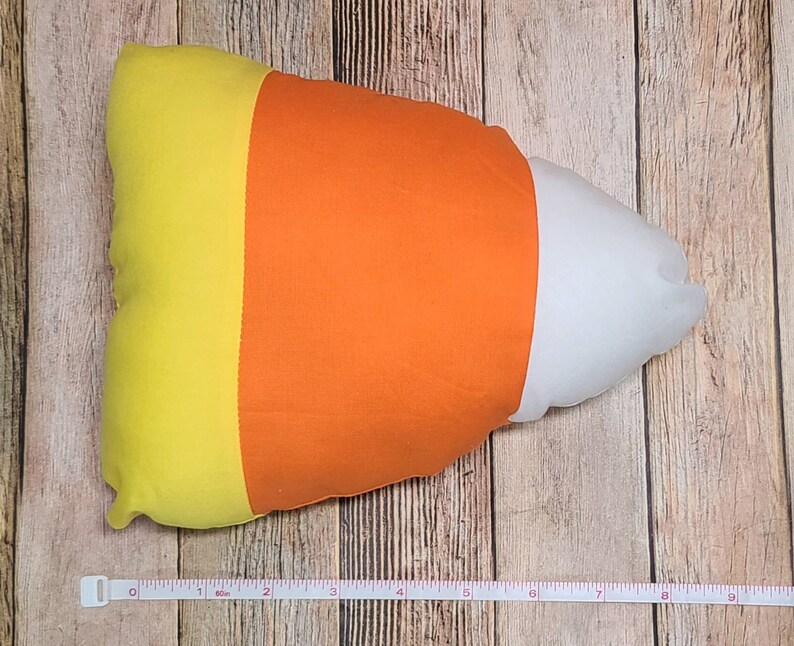 May include: A yellow, orange, and white candy corn shaped pillow. The pillow is about 18 inches long.