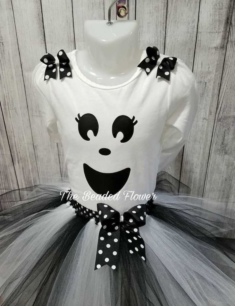 May include: A white tutu with black tulle layers and a black and white polka dot bow. A white shirt with a ghost face graphic and black and white polka dot bows on the shoulders. The shirt has the text "The Beaded Flower" on the bottom.