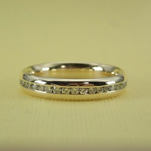 May include: A gold band ring with a single row of small diamonds set in a channel setting.