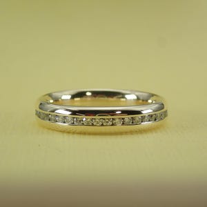 May include: A gold band with a row of small diamonds set in a white metal.