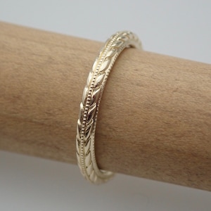 May include: A gold wedding band with a detailed leaf pattern.