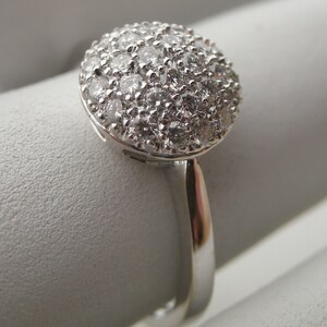 May include: A silver ring with a round, pave-set diamond top.