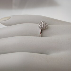 May include: A silver ring with a round, pave-set diamond center stone.