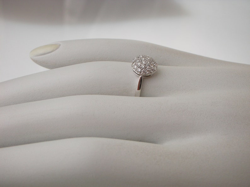 May include: A silver ring with a round, pave-set diamond center stone.