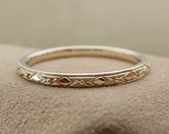 May include: A delicate gold wedding band with a diamond-shaped engraved pattern.