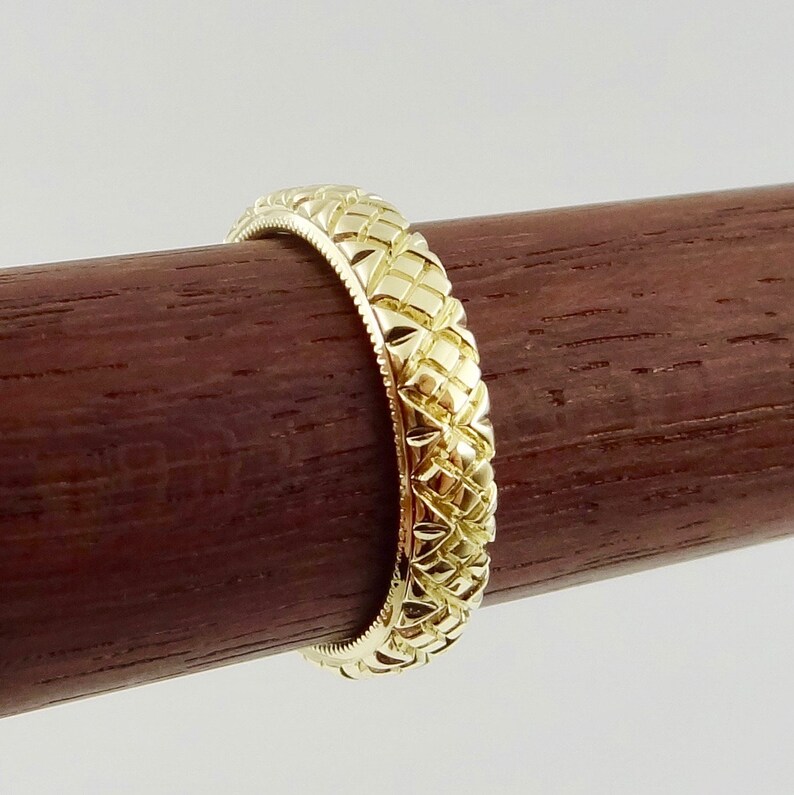 Puede incluir: Una banda de boda de oro con un patr&oacute;n de diamante texturizado.