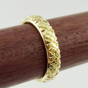Puede incluir: Una banda de boda de oro con un dise&ntilde;o tejido intrincado y detallado.