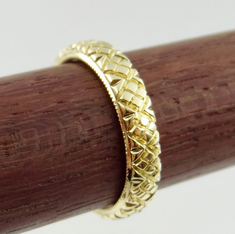 Puede incluir: Una banda de boda de oro con un dise&ntilde;o tejido intrincado y detallado.