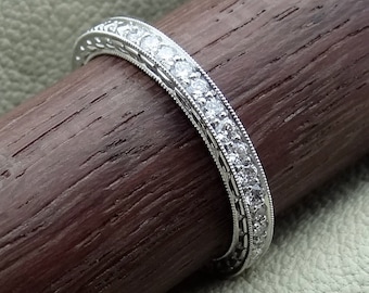 May include: A silver band with a row of small diamonds set in a delicate, intricate design.