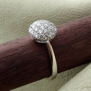 May include: A silver ring with a round, pave-set diamond center stone.