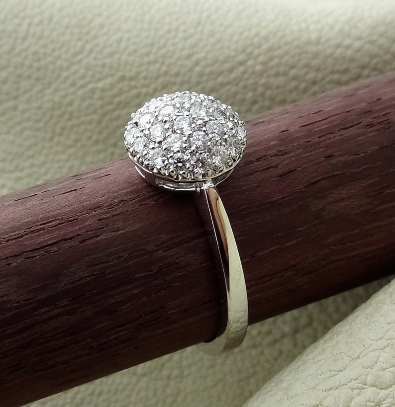 May include: A silver ring with a round, pave-set diamond center stone.