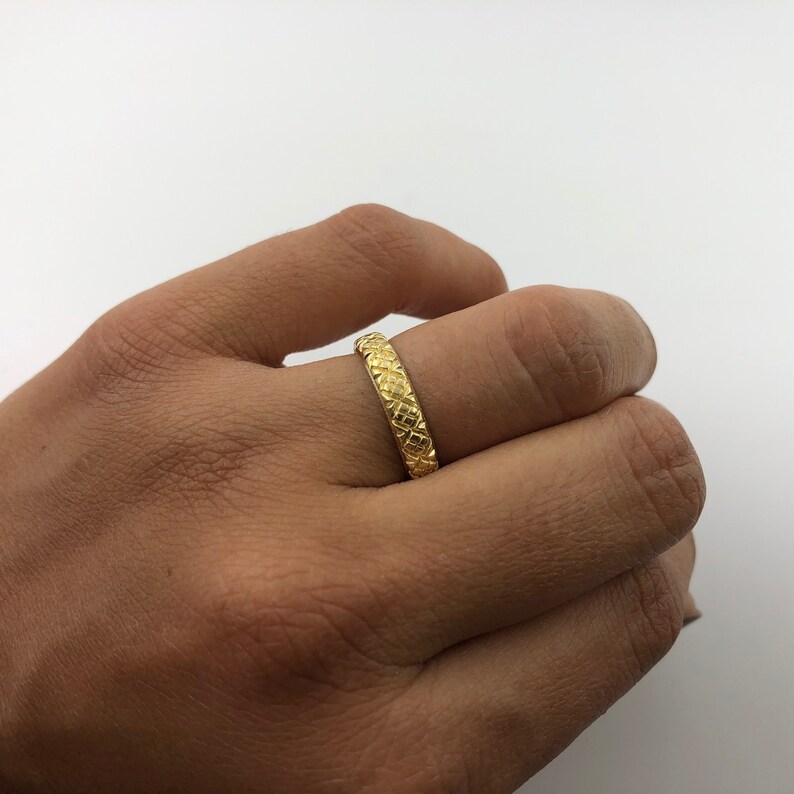 Puede incluir: Un anillo de banda de oro con un dise&ntilde;o texturizado. El anillo se usa en un dedo.