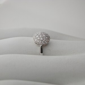 May include: A silver ring with a round, pave-set diamond top.
