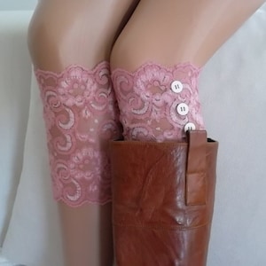 Può includere: Parigamba in pizzo rosa con bottoni bianchi. Le parigamba sono indossate sopra stivali in pelle marrone.