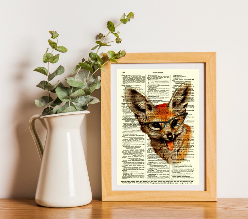 May include: A framed print featuring a whimsical illustration of a fox wearing glasses and a red hat, set against a vintage dictionary page. The artwork is in a wooden frame, with a white pitcher and green foliage in the background.