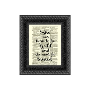 May include: A framed print with the quote "She was born to be Wild and she can't be tamed" in black script. The text is set against a vintage dictionary page background. The frame is black with a textured, crackled finish.