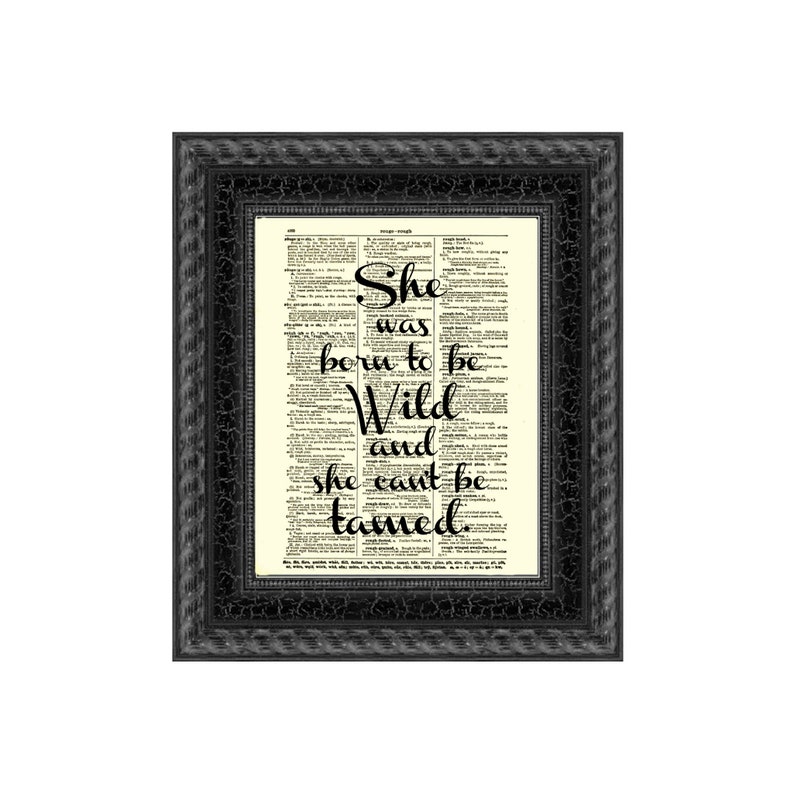 May include: A framed print with the quote "She was born to be Wild and she can't be tamed" in black script. The text is set against a vintage dictionary page background. The frame is black with a textured, crackled finish.