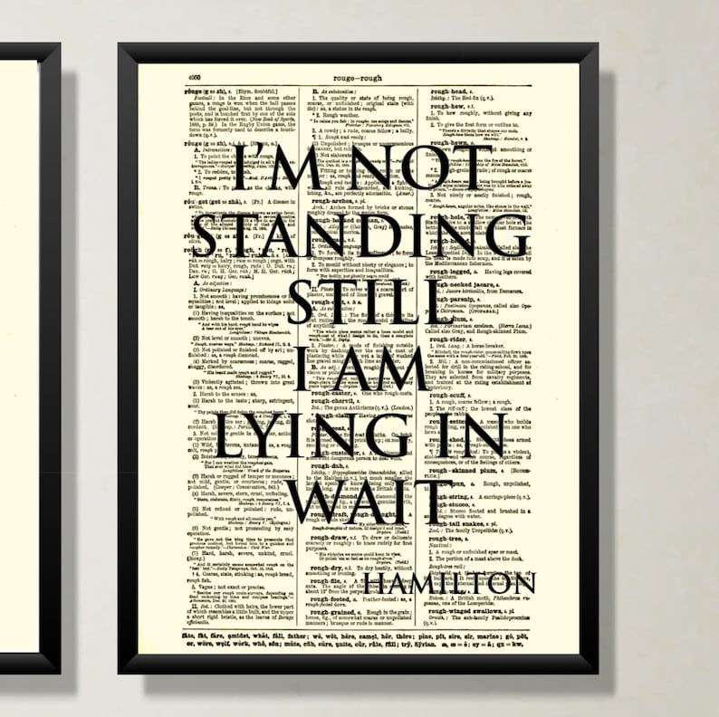 以下が含まれることがあります： 黒いフレームのアートプリント。テキスト「I'M NOT STANDING STILL I AM LYING IN WAIT HAMILTON」がヴィンテージ辞書ページに表示されています。