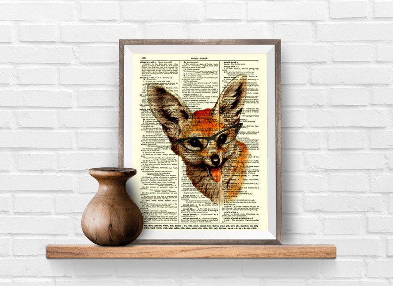 May include: Framed print featuring a whimsical fox illustration wearing glasses, set against a vintage dictionary page. The fox has orange and brown fur, with its tongue sticking out. The frame is a neutral color, and the print is displayed on a wooden shelf.