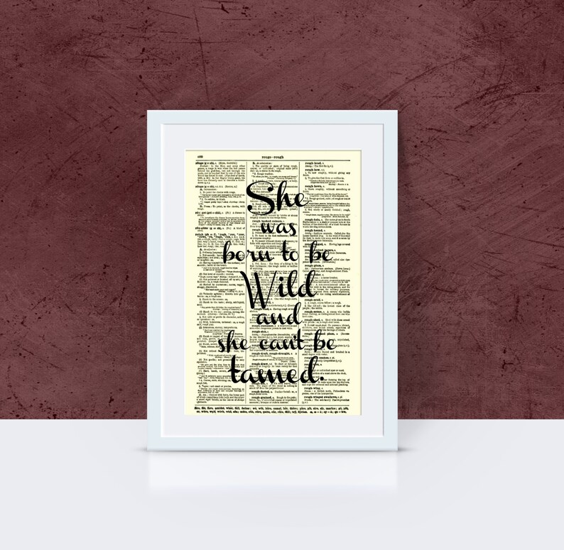 May include: A framed print featuring the quote "She was born to be Wild and she can't be tamed." The text is in black script over a vintage dictionary page, set in a white frame. The background is a deep burgundy.