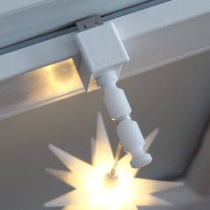 Könnte beinhalten: Weiße, an der Decke montierte Leuchte aus Kunststoff mit einem sternförmigen Schirm und einem weißen Kabel.