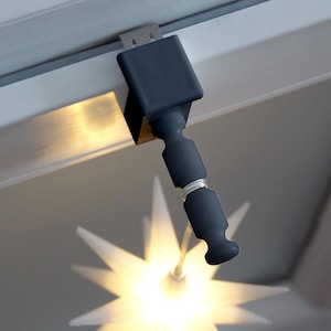 Op de afbeelding: Een donkergrijze, verstelbare LED-spot bevestigd aan een wit plafond. Het licht is naar beneden gericht en verlicht een stervormige armatuur eronder. De spot is gemonteerd met een metalen beugel.
