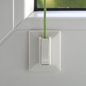 Puede incluir: Tirador de persiana blanco con un cordón verde. El tirador es rectangular con un botón central y está montado en una pared blanca. El cordón es verde y texturizado.