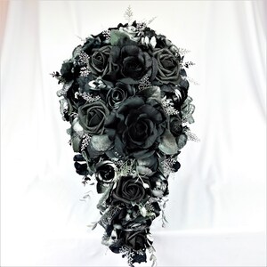 May include: A cascading bridal bouquet made of black roses and silver accents. The bouquet is arranged in a teardrop shape and features a variety of black roses, some with glitter accents.