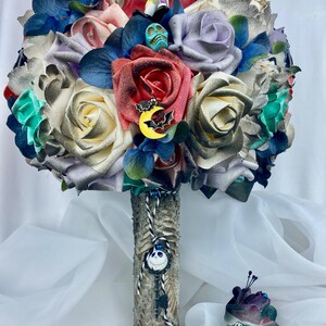 May include: A bouquet of artificial flowers in shades of purple, white, red, and green. The bouquet is decorated with various Halloween-themed charms, including a skull, a bat, and a key. The bouquet is tied with a black and white ribbon.