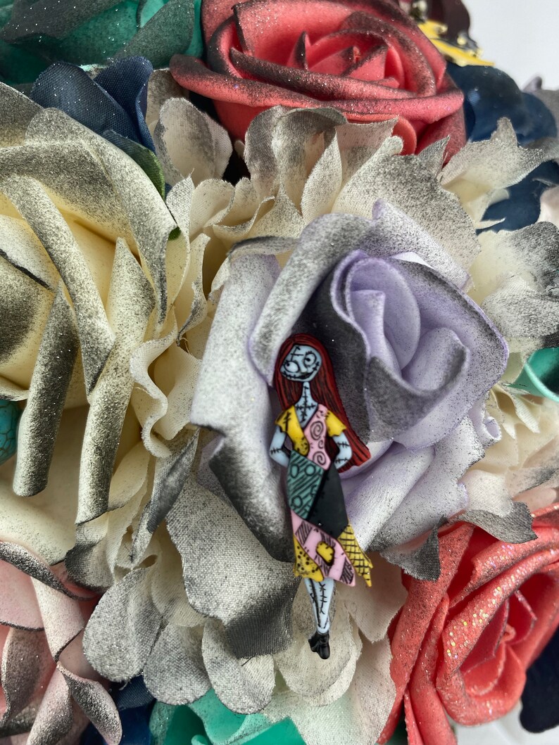 May include: A bouquet of artificial flowers in shades of white, pink, red, and green. A small figurine of Sally from the Nightmare Before Christmas is attached to the bouquet.