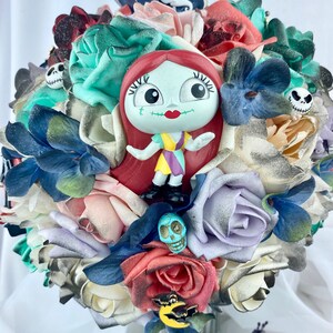 May include: A bouquet of artificial flowers in various shades of pink, white, blue, and green. The bouquet features a small plastic figurine of Sally from the Nightmare Before Christmas, a skull, and a bat charm.