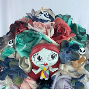 May include: A bouquet of artificial flowers in shades of red, pink, blue, and green. The bouquet features a small plastic figurine of Sally from the Nightmare Before Christmas, a skull, and a ghost.