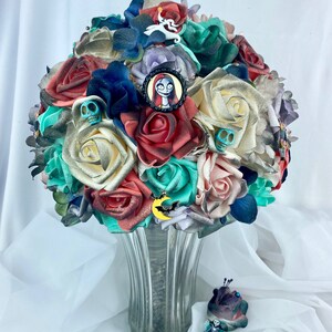 May include: A bouquet of artificial flowers in shades of red, white, green, and blue. The bouquet features a variety of flowers, including roses, orchids, and lilies. The bouquet is decorated with a variety of embellishments, including skulls, bats, and a character from the movie The Nightmare Before Christmas. The bouquet is arranged in a clear glass vase.