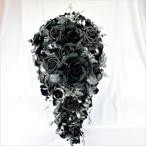 May include: A cascading bridal bouquet made of black roses and silver accents. The bouquet is arranged in a teardrop shape and features a variety of black roses, some with glitter accents.