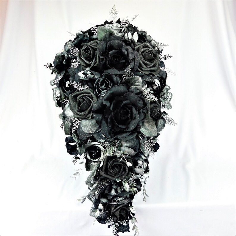 May include: A cascading bridal bouquet made of black roses and silver accents. The bouquet is arranged in a teardrop shape and features a variety of black roses, some with glitter accents.