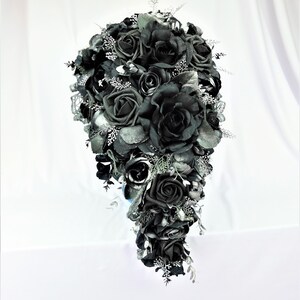 May include: A cascading bridal bouquet made of black roses with silver accents. The bouquet is made of artificial flowers and is perfect for a gothic wedding.