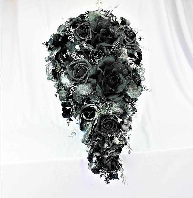 May include: A cascading bridal bouquet made of black roses with silver accents. The bouquet is made of artificial flowers and is perfect for a gothic wedding.