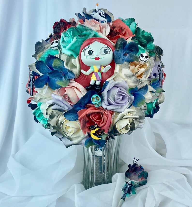 May include: A bouquet of faux flowers in shades of white, cream, green, blue, and red. The bouquet features a small plastic figurine of Sally from the Nightmare Before Christmas, a skull, and a bat.
