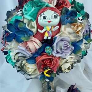 May include: A bouquet of faux flowers in shades of red, white, blue, green, and purple. The bouquet features a small plastic figurine of Sally from the Nightmare Before Christmas, a few skull-shaped charms, and a bat charm with a crescent moon.