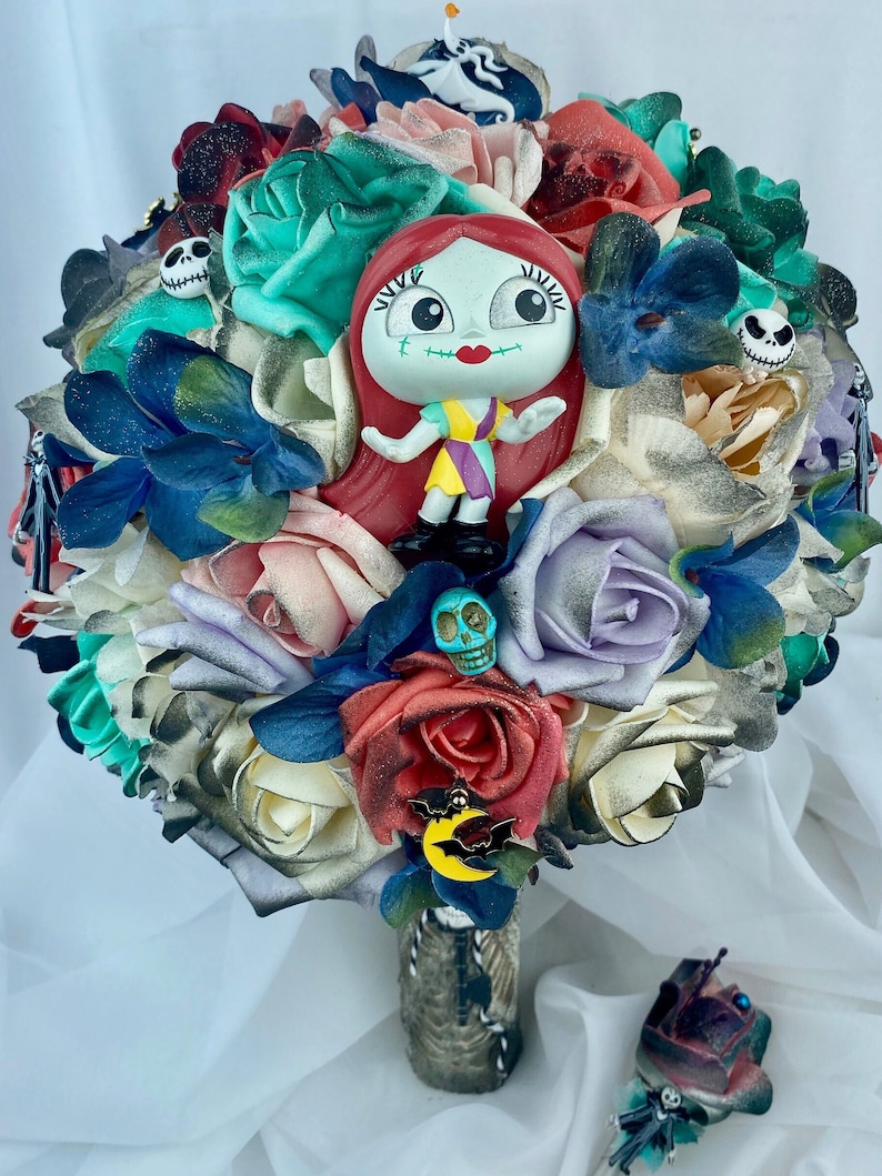 May include: A bouquet of faux flowers in shades of red, white, blue, green, and purple. The bouquet features a small plastic figurine of Sally from the Nightmare Before Christmas, a few skull-shaped charms, and a bat charm with a crescent moon.