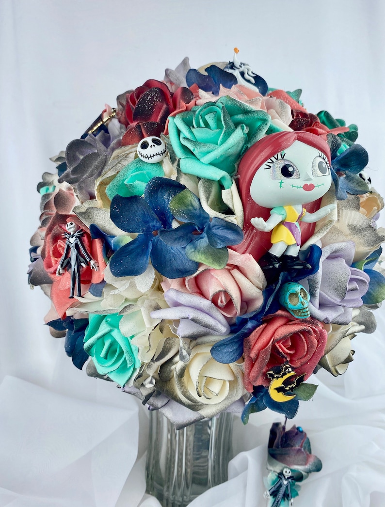 May include: A bouquet of artificial flowers in shades of red, white, blue, and green. The bouquet features a variety of flowers, including roses, hydrangeas, and other blooms. The bouquet is decorated with small figurines of characters from the movie "The Nightmare Before Christmas."
