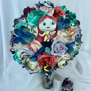 May include: A colorful bouquet of artificial flowers with a small plastic doll of Sally from the Nightmare Before Christmas movie. The bouquet is decorated with various Halloween-themed charms, including skulls and bats.
