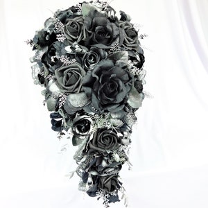 May include: A cascading bridal bouquet made of black roses with silver glitter accents. The bouquet is arranged in a teardrop shape and features a variety of black roses, some with a more velvety texture and others with a more satin finish.