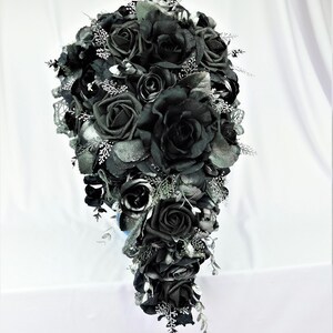 May include: A cascading bridal bouquet with black roses and silver accents. The bouquet is made of artificial flowers and is perfect for a gothic wedding.