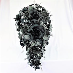 May include: A cascading bridal bouquet made of black roses and silver foliage. The bouquet is arranged in a teardrop shape and features a variety of black roses, some with glitter accents.
