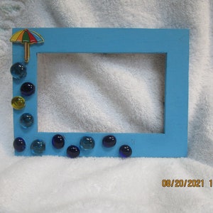 Könnte beinhalten: Ein hellblauer Bilderrahmen, der mit bunten Glasperlen und einem kleinen Regenschirm verziert ist. Der Rahmen ist bereit, ein Foto aufzunehmen.