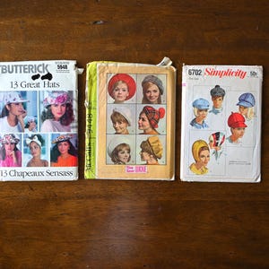 May include: Three vintage sewing pattern booklets featuring hat designs. The booklets are titled "13 Great Hats," "Quicke," and "Simplicity." The covers display illustrations of various hat styles, including berets, cloches, and caps, in a range of colors and patterns.